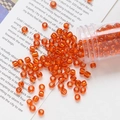 Close-up of 4mm orange glass beads with gold foil spilled from a clear plastic tube - Orange Red