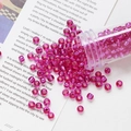 Macro detail of 4mm rose pink glass seed beads pouring from a tube for DIY jewelry making - Rose Pink