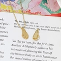 Gros plan artistique de pendentifs mains dorés et d'un collier délicat sur un livre - 5# Geste OK