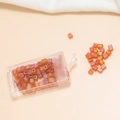 Macro view of 4mm orange-pink iridescent square hole glass beads in a clear box - Orange