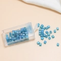 Macro detail of iridescent blue 4mm glass cube beads with central hole in storage box - Mint Green