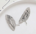 Macro-opname van zilveren vleugelbedeltjes voor DIY-sieraden op een witte keramische schaal - Zilver