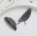 Macro-opname van gunmetal veren hangers voor DIY-sieraden op een wit bordje - Gunmetal