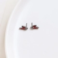 Detail of red enamel wing earrings on a white ceramic plate with a metallic finish - Gun Black Rabbit Ear