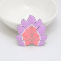 Détail d'une broche florale en émail violet et rose posée sur un bol en céramique blanc - Socle Platine Renard à Neuf Queues