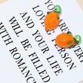 Detailed close-up of orange glass fruit beads with green hooks for DIY jewelry making - Pineapple