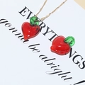 Macro detail of a red glass heart cherry pendant necklace with green leaf and golden chain - Heart Pepper