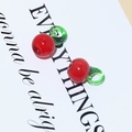 Macro detail of red glass cherry beads with green stems for DIY jewelry making - Tomato