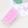 Macro detail of soft pink macaron glass seed beads in a transparent plastic storage box - Sakura Pink