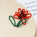 Dettaglio macro di un ciondolo a fiore fatto a mano con perline rosse e verdi - Rosso