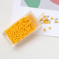 Macro shot of 3mm bright yellow macaron seed beads spilling from a clear storage box - Orange