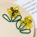 Macro view of handmade bead-woven yellow flower earring accessory on a beige stand - Yellow