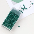 Detail of dark green macaron glass seed beads in a transparent plastic storage box - Dark Green