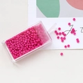 Detailed view of pink macaron glass seed beads in a slide-open plastic organizer box - Rose Red