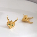 Macro detail of gold-plated dragon head earrings with green gemstone eyes and scales - Gold