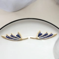 Detail of gold-plated wing earrings with dark blue enamel and glitter on white ceramic - Devil Wing Gold