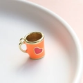 Dettaglio di un ciondolo a tazza arancione con cuore e bordi in metallo dorato - Tazza Arancione