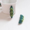Detailansicht handgefertigter Erbsenschoten aus Filzwolle mit drei grünen Erbsen in einer Tasse - Erbsenschote / 1 Stück