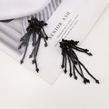 Macro detail of black beaded tassel earrings with faceted crystals on a white fabric background - Black