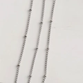 Macro shot of silver beaded chain links featuring smooth metal accents and polished oval rings - Rhodium Plated