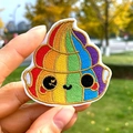 Detalle de parche bordado con diseño de arcoíris sonriente sostenido a mano al aire libre - Estilo Caca Arcoíris (PE5779CT)