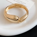 Close-up of a chunky gold metallic bangle with a unique teardrop overlapping design. - Water Drop Overlapping Shape (78#) / Gold