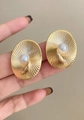 Dettaglio macro di orecchini ovali dorati con texture a spirale e perla centrale. - Oro