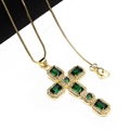 Detailed macro view of a gold cross pendant with emerald stones and zircon accents - Green