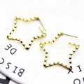 Macro shot of gold star-shaped earrings with textured wavy metal surface on a white page - Star Shape Style (1)