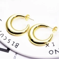 Detailed view of chunky golden C-shaped hoop earrings on a decorative white plate - Polished C-Shape (6)