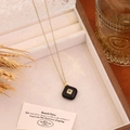 Close-up detail of a square black pendant necklace displayed in a white velvet jewelry box. - Black Agate