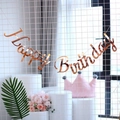 Roségoldenes Happy Birthday Banner mit Schreibschrift an einer weißen Gitterwand - Roségold