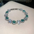 Close-up detail of a luxury emerald green and clear zircon floral bracelet on beige velvet. - Oval Gemstone Petal Style