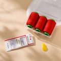 Close-up of red sewing threads, needles, and a yellow threader in a clear tool kit - Red