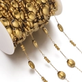 Macro detail of golden oval bead and triple mini bead chain on white plastic spool - Approx 6*7.5mm Oval, 1 Meter / Gold