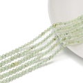 Dettaglio di perle sfaccettate in pietra naturale verde chiaro su un piatto bianco - Prehnite