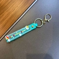 Detail of green PVC keychain featuring The Sunshine Unicorn print and golden metal clip - Unicorn Rainbow Strap / Green