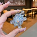 Handheld view of a transparent turtle charm filled with colorful iridescent glitter stars - Small Glow Flash Turtle / 1 Piece / White