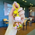 Close-up of a liquid-filled pig keychain with floating glitter and a yellow bell charm - Colored Hardware Style / Gold