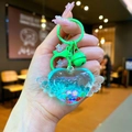 Detail of heart-shaped liquid keychain with wings, sequins, and a green bell accessory - Lobster Clasp Style / Green