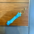 Blue silicone Sakura keychain with floral charms and golden metal clip on wood surface - Blue