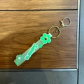 Detail of green Sakura PVC wristlet strap with golden metal clasp on a wooden background - Green