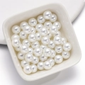 Close-up of high-luster white round loose glass pearls in a white ceramic dish - 3mm / White