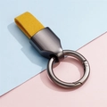 Details von gelbem Leder-Schlüsselanhänger mit grauen Metallteilen auf pastellfarbenem Hintergrund - Gunmetal Gelb