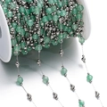 Detailed close-up of green faceted stone beads and silver metal chain on a white spool - Steel Style 04