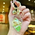 Close-up of resin seashell keychain with golden bell and sand-filled ocean pendant - Conch Pendant (Gold Buckle) / Green