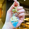 Detailed close-up of a conch-shaped acrylic keychain with blue sequins and shells - Conch Pendant (Gold Buckle) / Blue