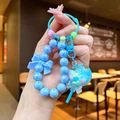 Detalle de llavero de cuentas azul claro con lazo y colgante de lentejuelas en la mano - Estilo Piruleta / Azul