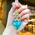 Détail d'un porte-clés fraise iridescent avec feuille dorée et dégradé de couleur bleu-vert - Fraise Électroplaquée Bleue Or