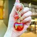 Detailed shot of two red translucent apple charms with rainbow finish on a gold keychain - Gold Hardware Red Electroplated Persimmon